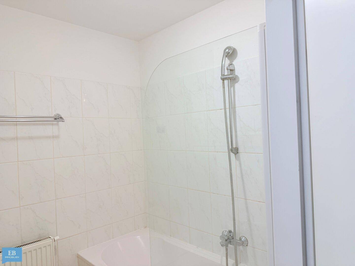 Badezimmer mit weiß gefliesten Wänden, Badewanne und Duscharmatur, bereit zur Nutzung.