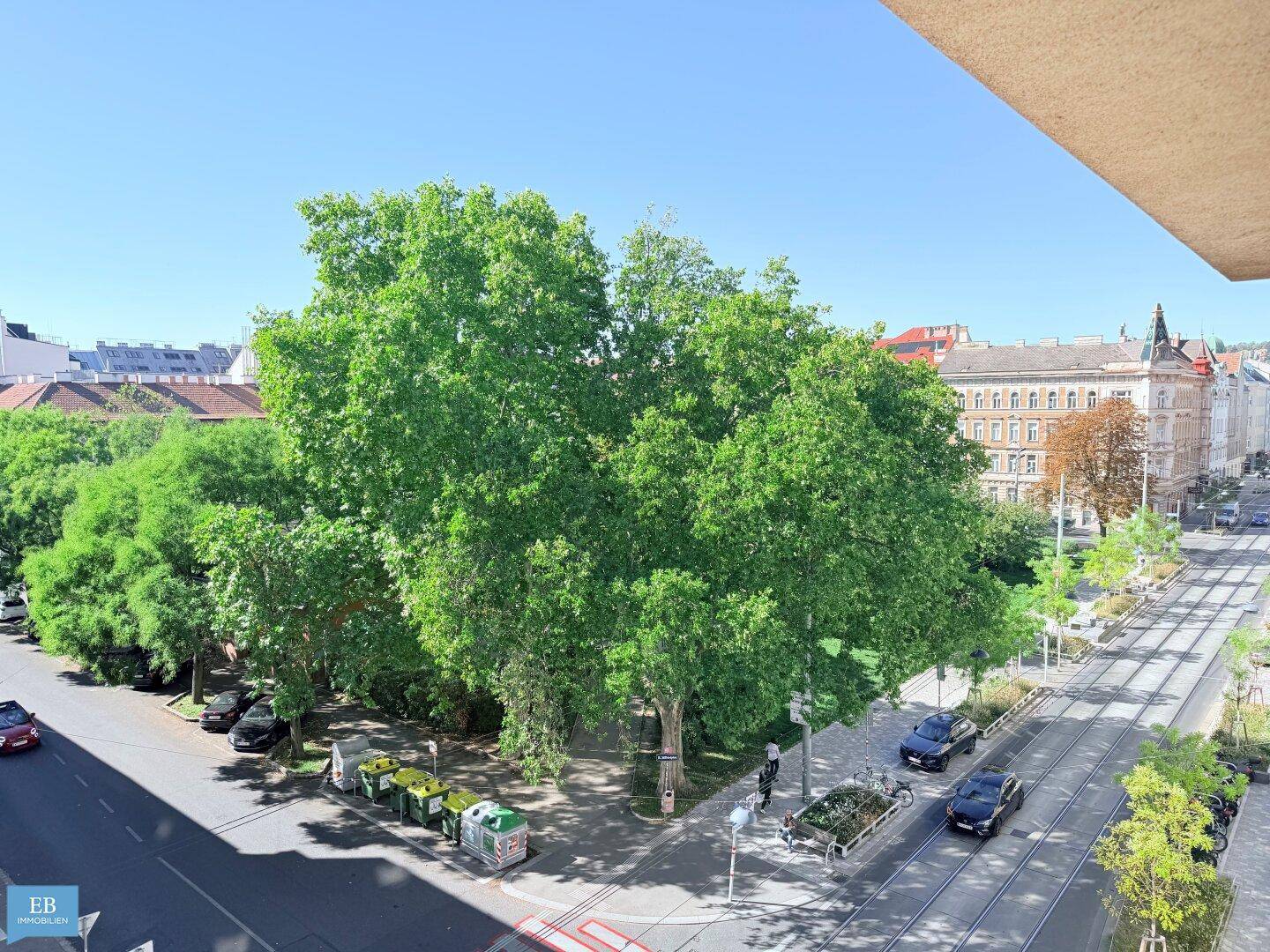 Blick von oben auf eine belebte Straße mit vielen Bäumen, Straßenbahnen und Gebäuden in der Ferne.