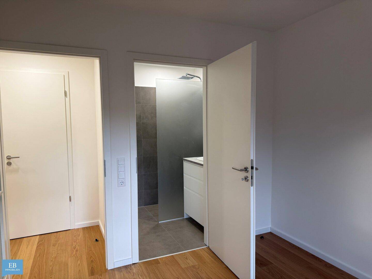 Flur mit Holzboden und Zugang zu einem modernen Badezimmer mit Dusche.