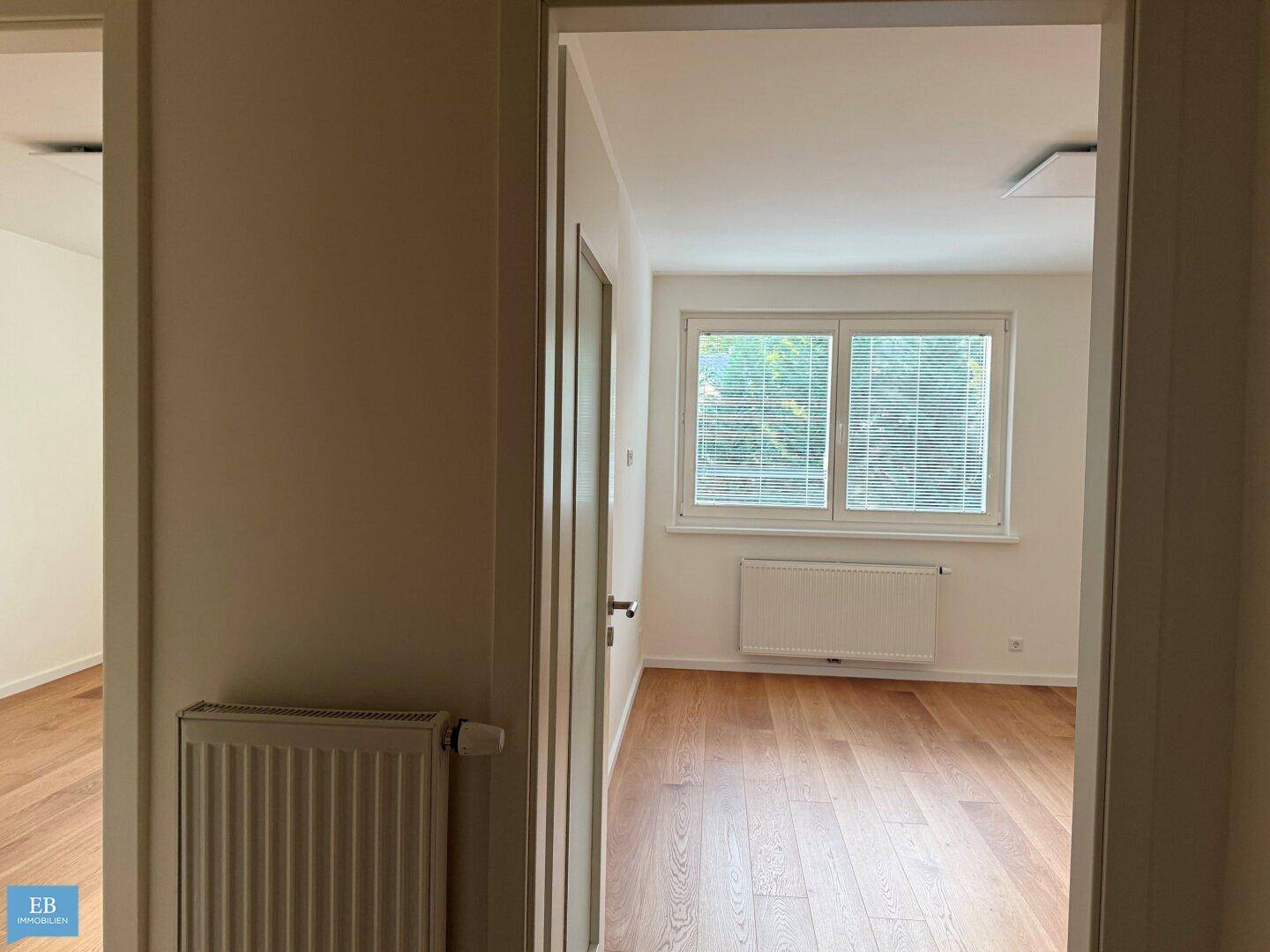 Heller Flur mit Holzboden, der zu weiteren Zimmern und einem Fenster führt.