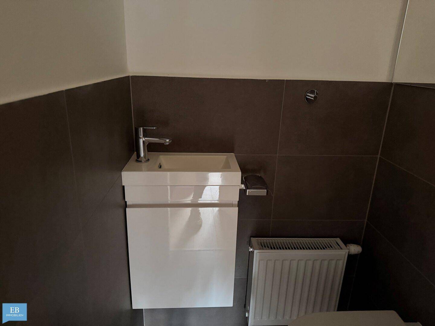 Kleines, modernes Gäste-WC mit Waschtisch und dunklen Wandfliesen.