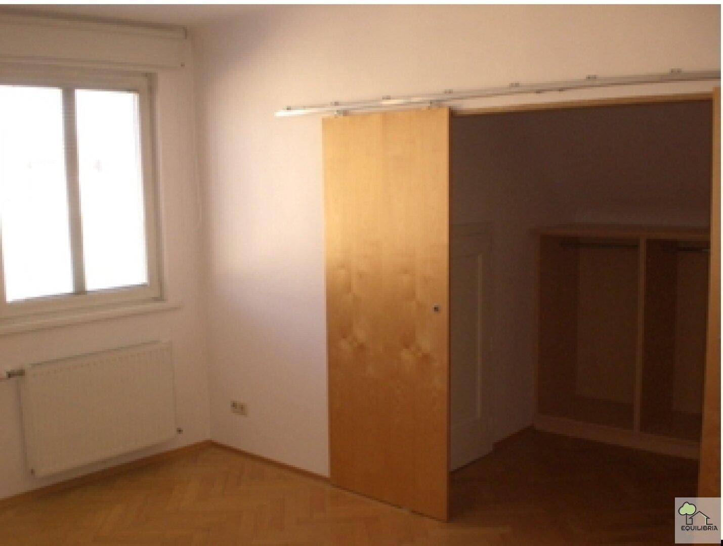 Schlafzimmer mit Parkettboden und Schiebetür, die zu einem begehbaren Kleiderschrank führt.