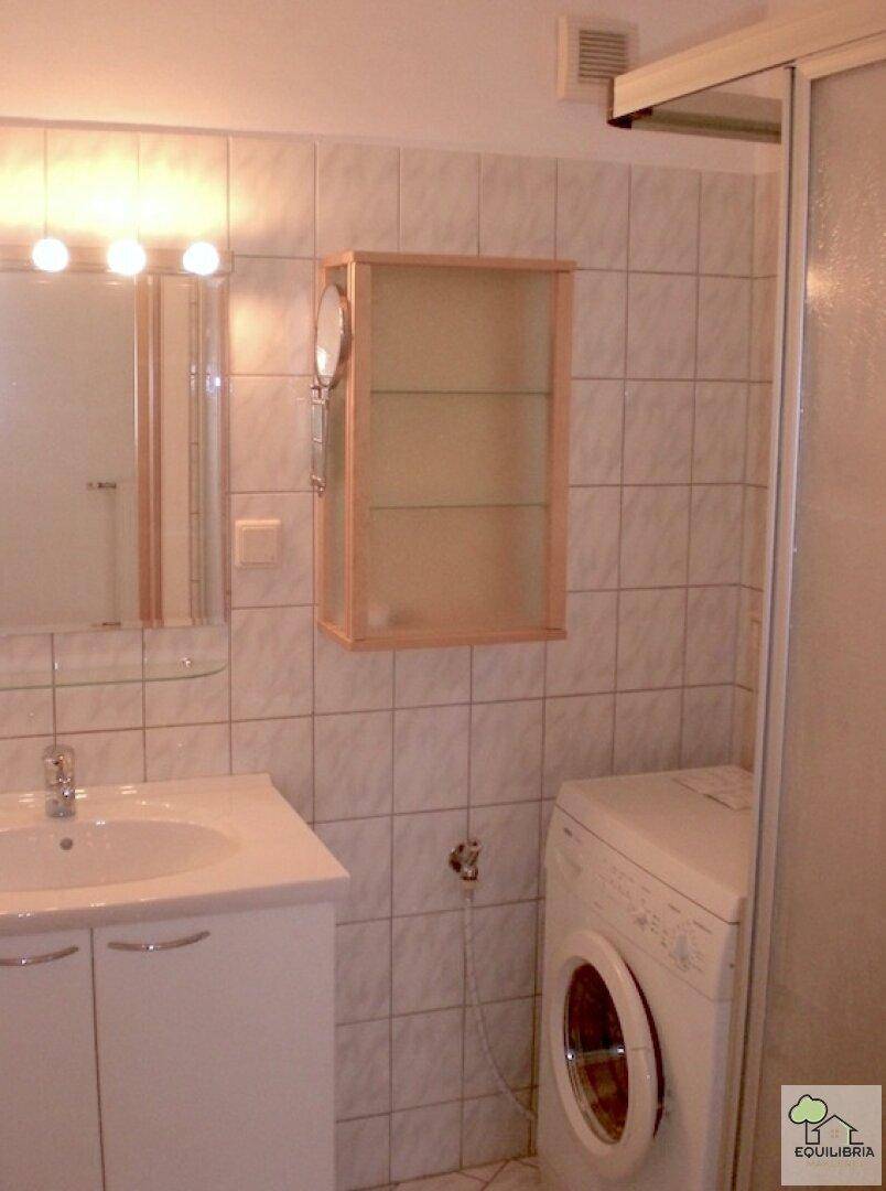 Gefliestes Badezimmer mit Waschbecken, Spiegelschrank und Duschkabine, inklusive Waschmaschine.