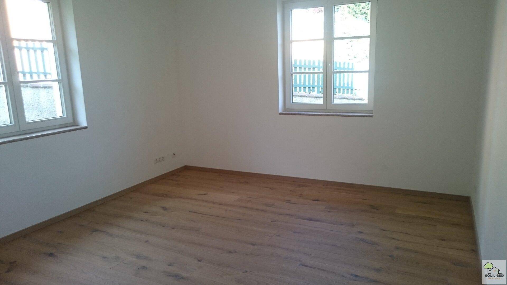 Leeres Zimmer mit Holzboden und Fenster, bereit für individuelle Gestaltung.