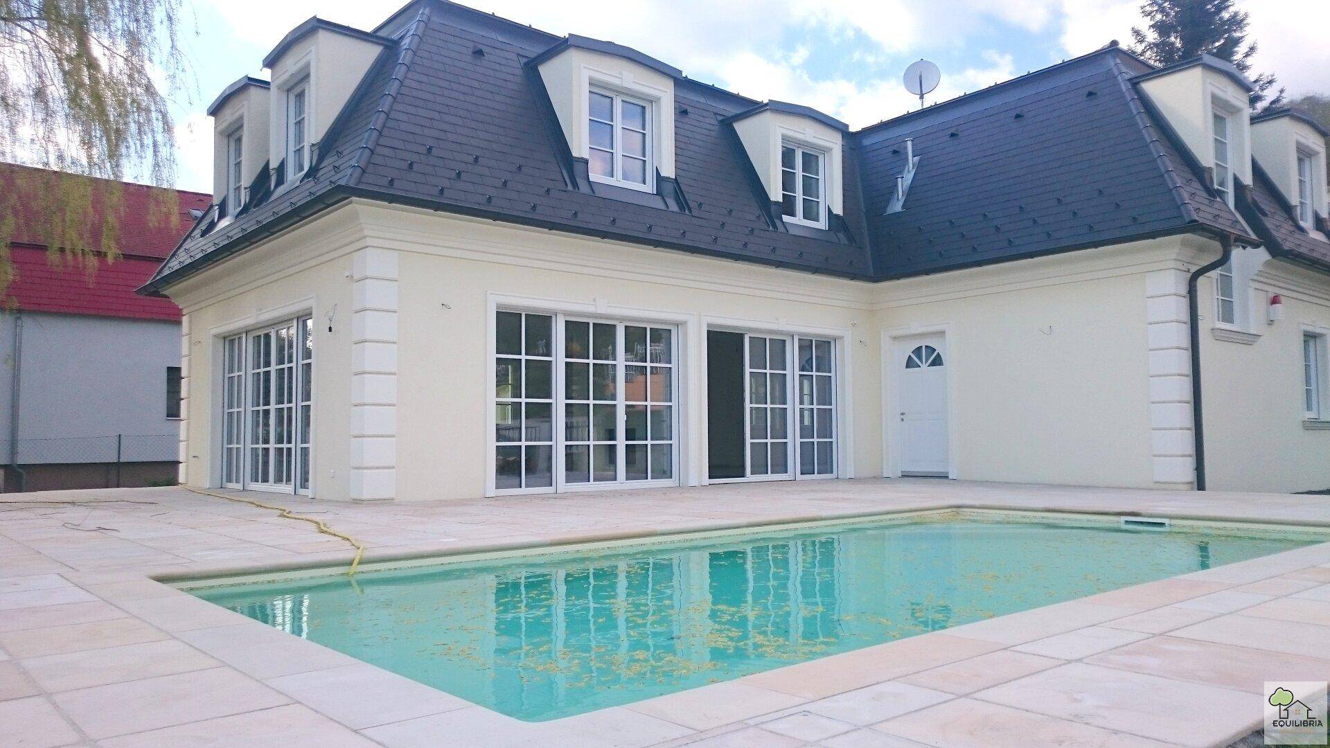 Moderne Villa mit elegantem Mansarddach, Pool und gepflegtem Rasenbereich.
