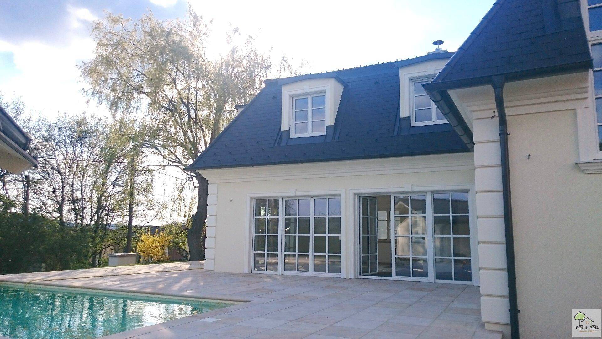 Sonnenbeschienene Hausfassade mit großen Fenstern und direktem Zugang zum Pool.