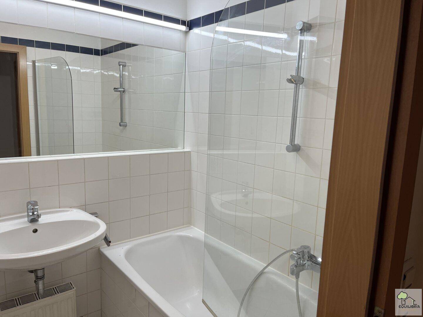 Badezimmer mit Badewanne, Duschvorrichtung und Waschbecken, ausgestattet mit weißen Fliesen.