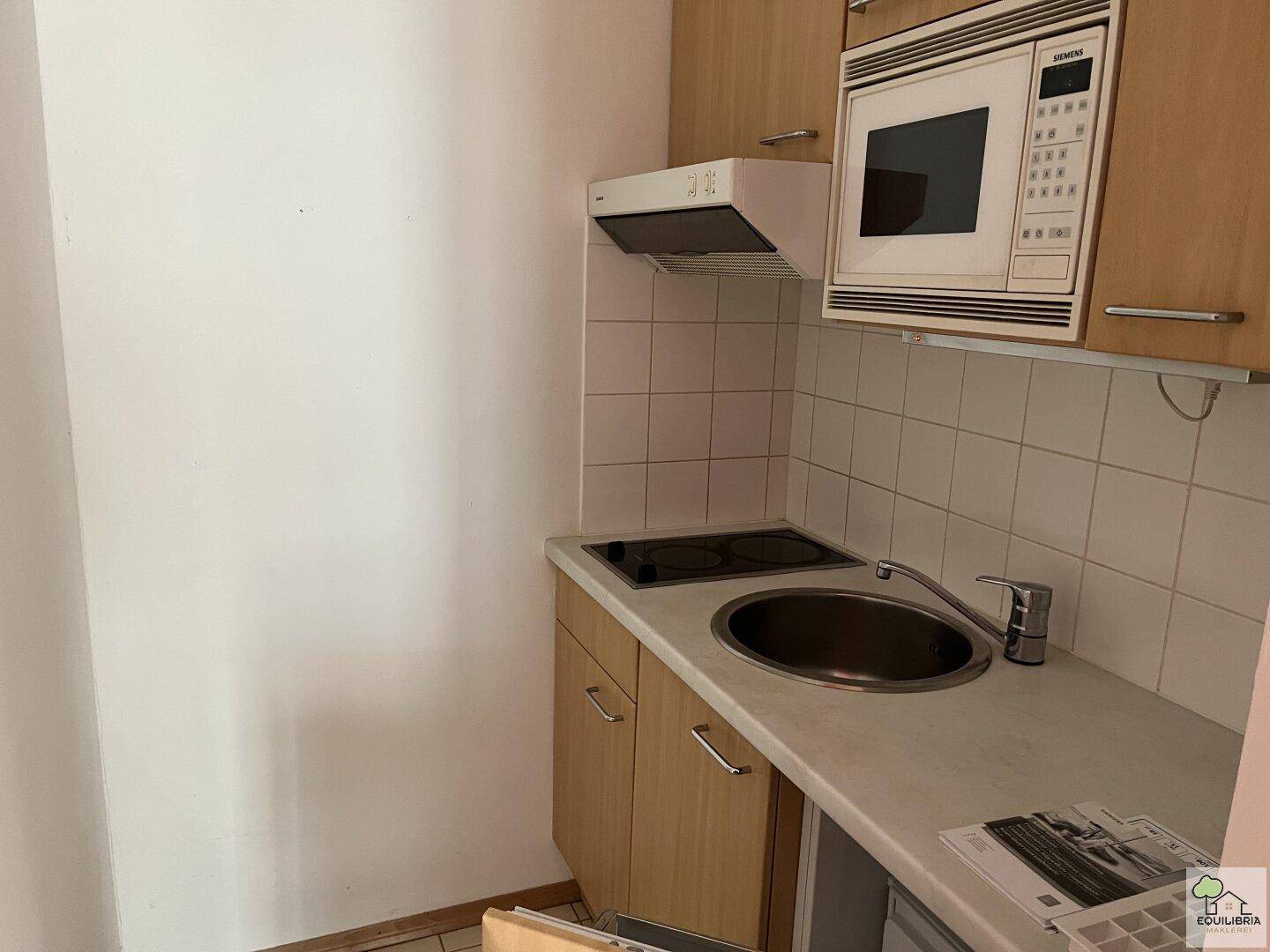 Kompakte Küchenzeile mit Spüle, Kochfeld und Mikrowelle, ideal für kleine Wohnungen.