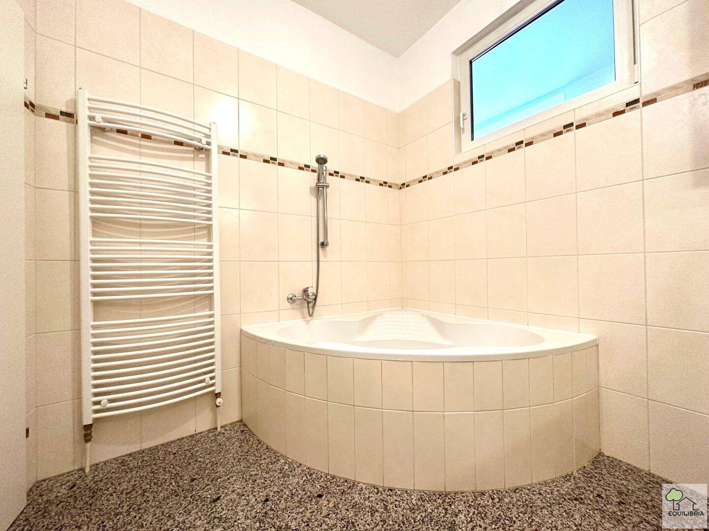Badezimmer mit Eckbadewanne, beheiztem Handtuchhalter und einem Fenster für Belüftung.