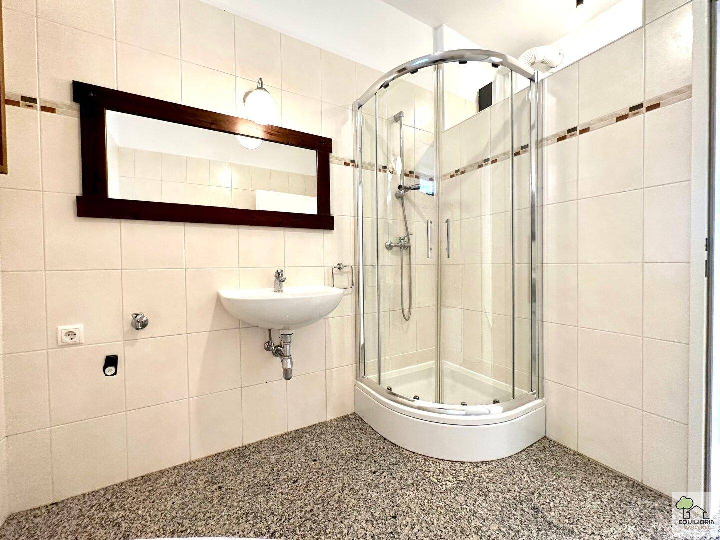 Badezimmer mit Duschkabine, Einzelwaschbecken und einem großen Spiegel.