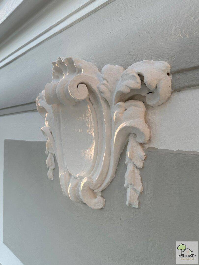 Detailaufnahme einer kunstvollen Stuckverzierung an der hellgrauen Fassade des historischen Gebäudes.