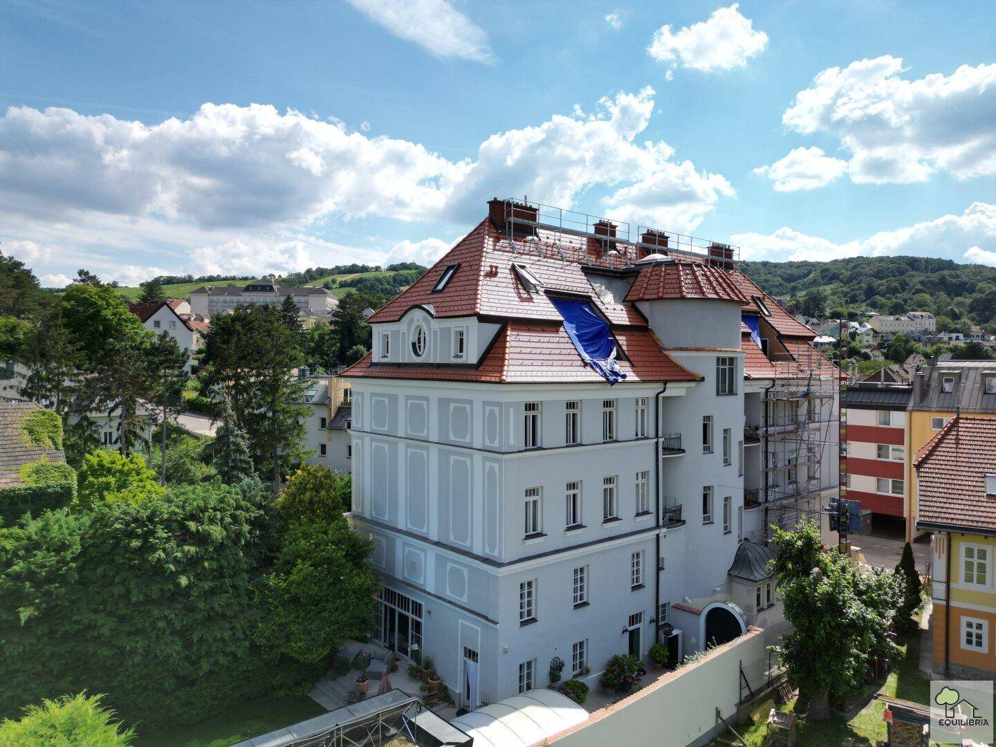Seitenansicht des historischen Gebäudes mit Gerüst und blauer Plane auf dem Dach, was auf Renovierungsarbeiten hindeutet.