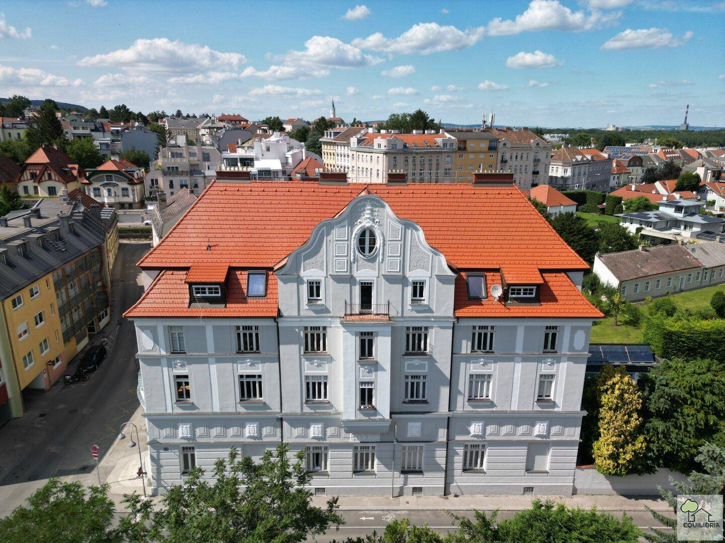 Frontansicht des historischen Gebäudes mit rotem Dach und detaillierter Fassade in einer städtischen Umgebung.
