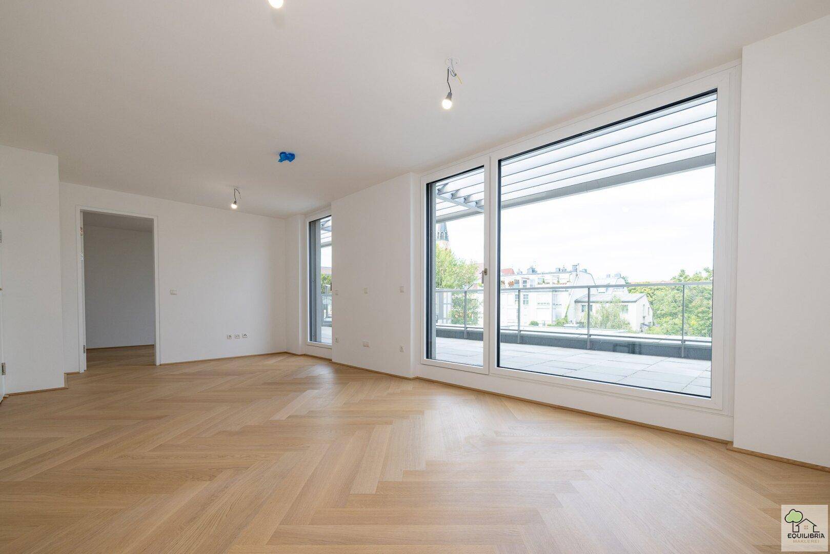 Helles, leeres Wohnzimmer mit Fischgrätparkett und großen Fenstern zum Balkon.