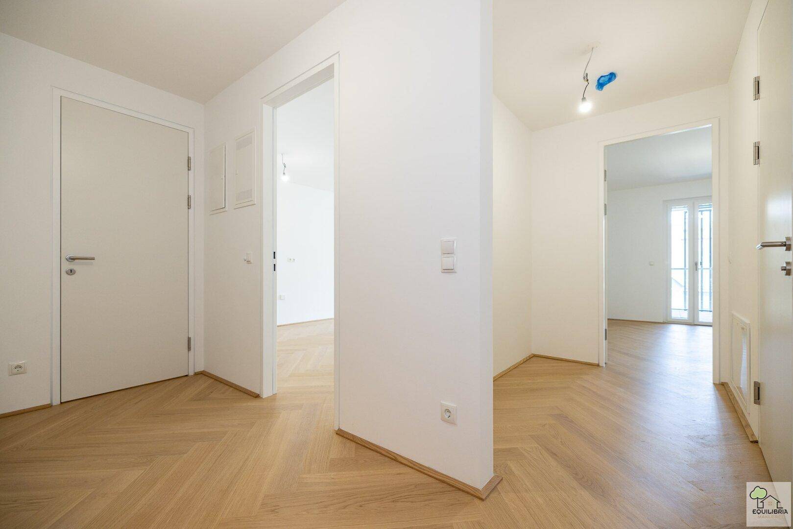 Heller Flur mit Fischgrätparkett und mehreren Türen, der verschiedene Räume verbindet.