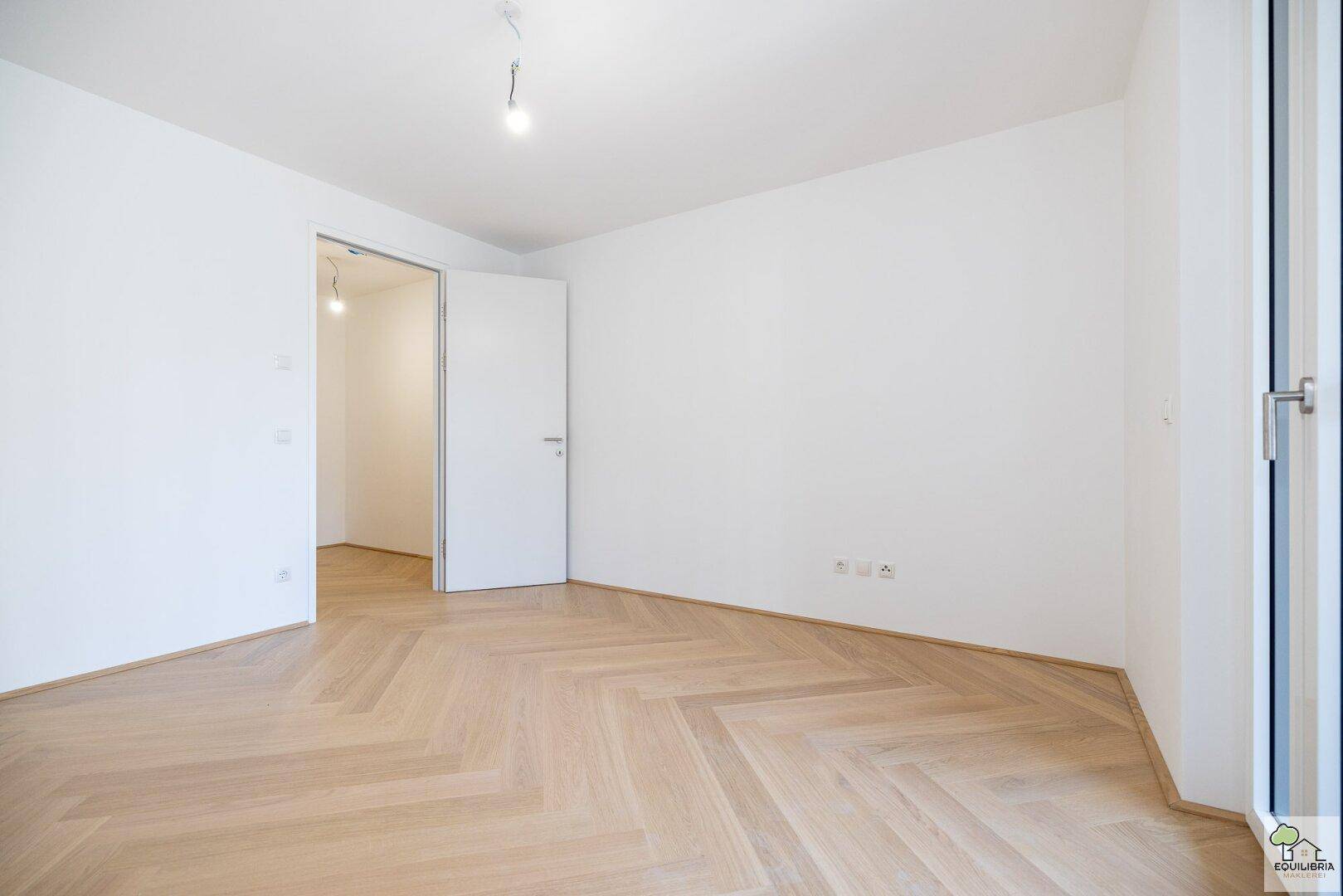 Helles, leeres Zimmer mit elegantem Fischgrätparkett und weißen Wänden, bereit zum Einzug.