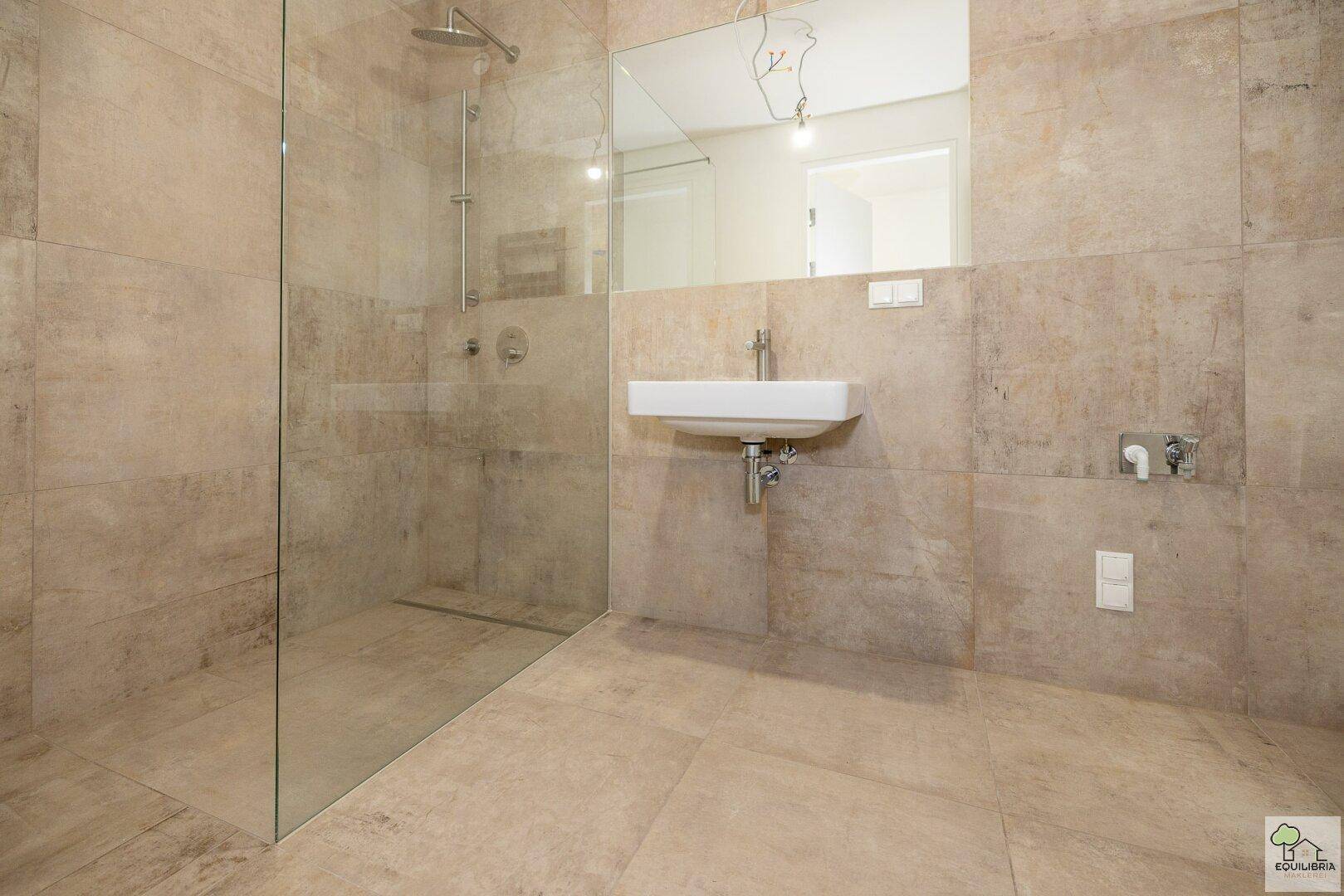 Modernes Badezimmer mit großformatigen Fliesen, begehbarer Dusche und wandmontiertem Waschbecken.
