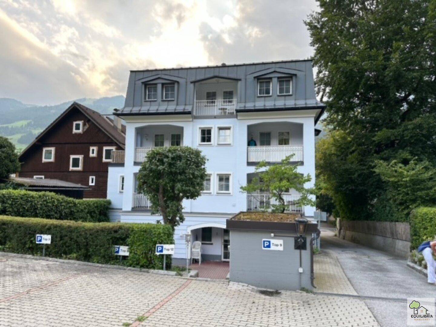 Ansicht des Gebäudes von der Seite mit Parkplätzen und umliegender grüner Landschaft.