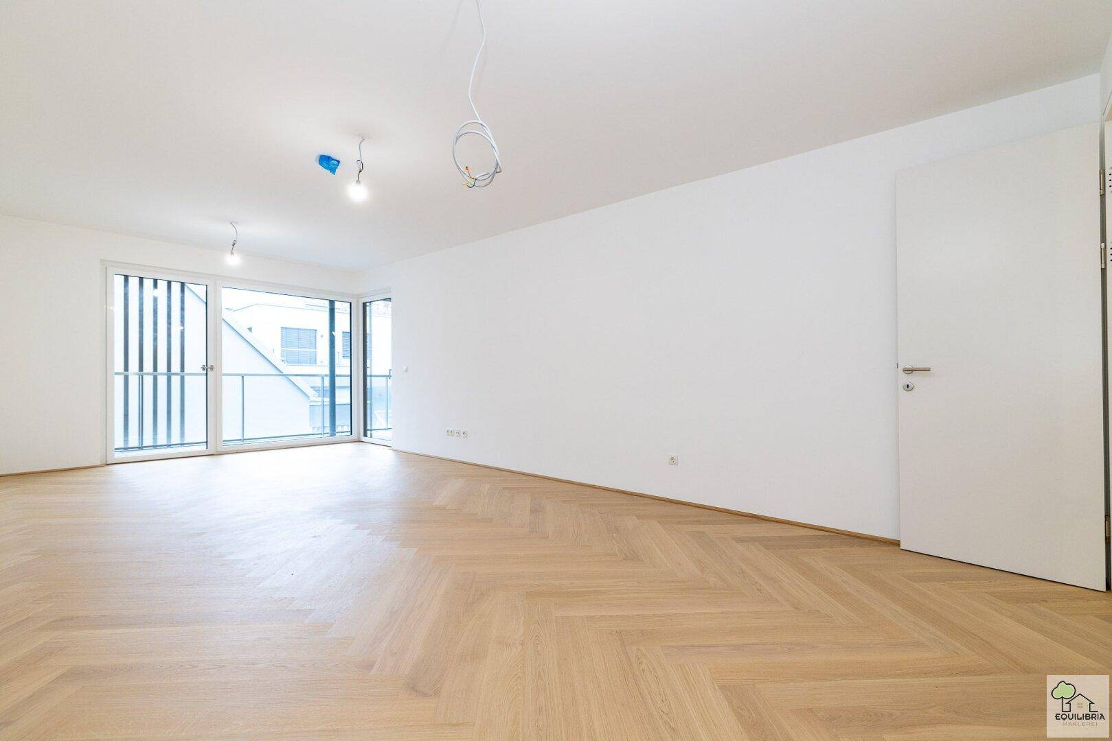 Heller, leerer Raum mit elegantem Fischgrätparkett und Zugang zu einem Balkon.