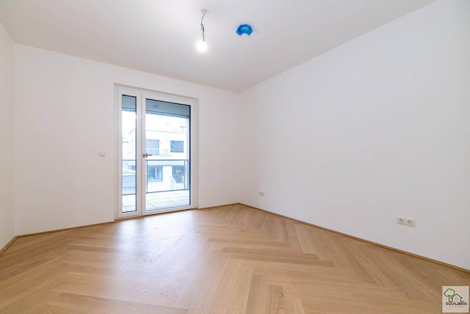 Helles Schlafzimmer mit Fischgrätparkett und direktem Zugang zu einem Balkon.