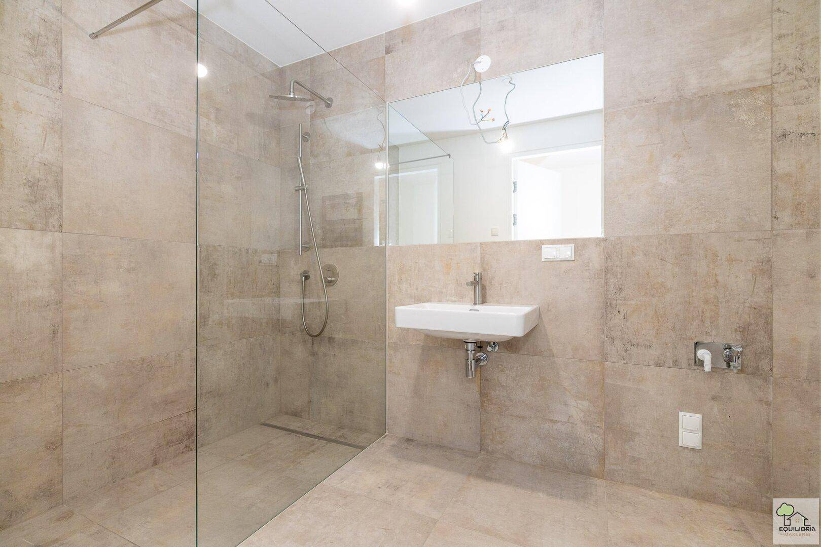 Modernes Badezimmer mit großformatigen Fliesen, begehbarer Dusche und Wandwaschbecken.