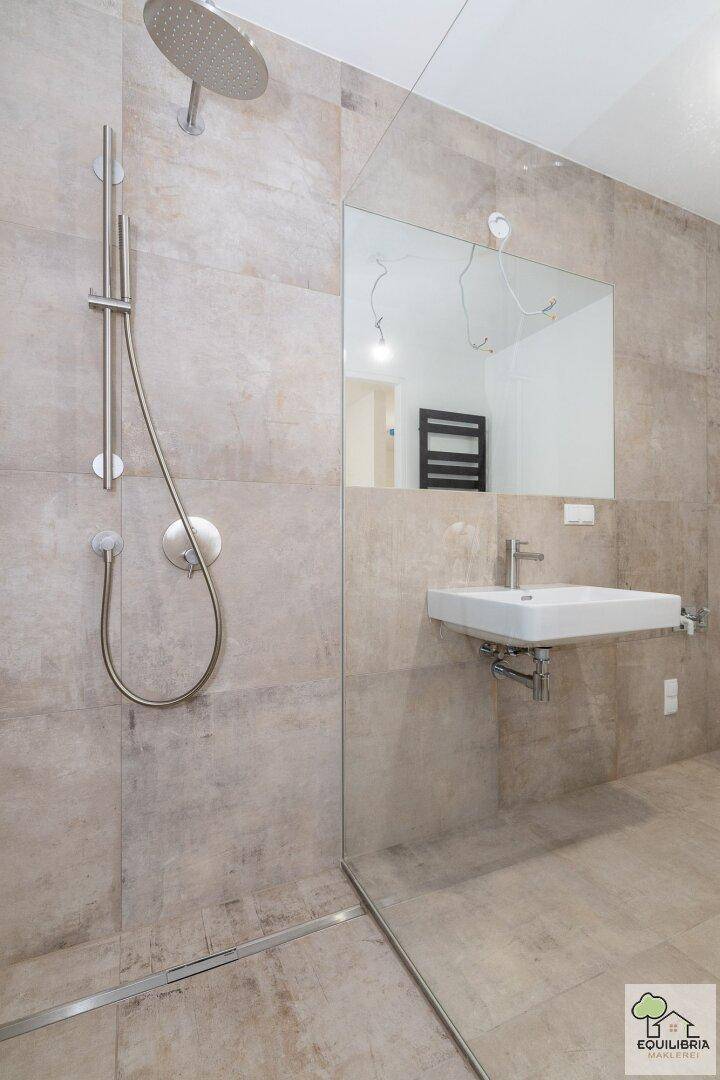 Detailansicht der begehbaren Dusche mit Regenduschkopf und modernem Waschbecken im Bad.