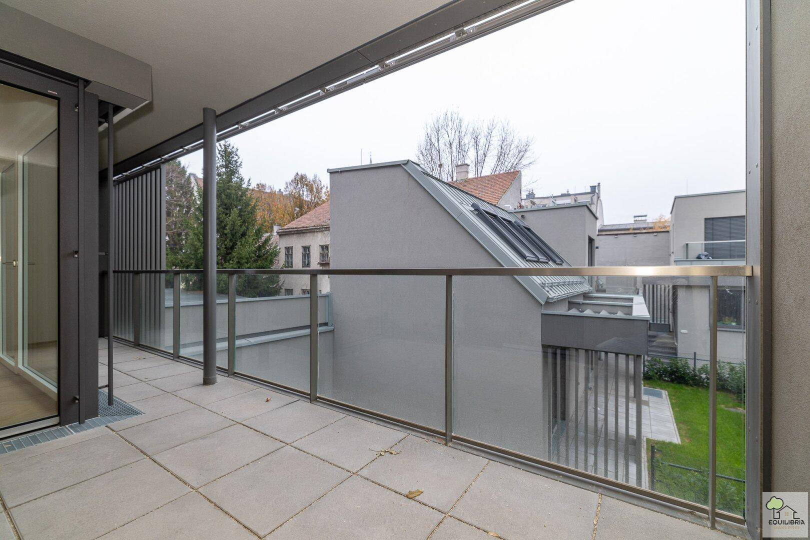 Geräumiger Balkon mit Glasgeländer und Blick auf moderne Gebäude und Grünflächen.