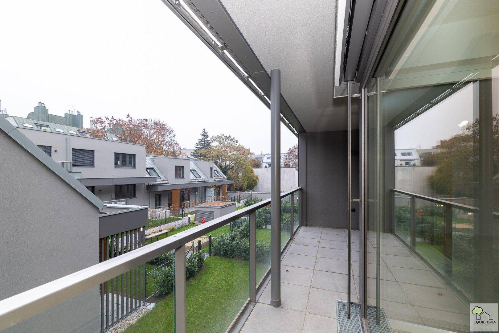 Balkon mit Blick auf den gepflegten Gemeinschaftsgarten mit Rasen und Spielbereich.