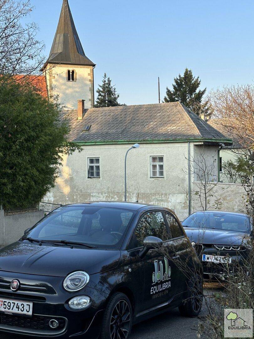 Blick auf die Straße mit parkenden Autos und einer Kirche im Hintergrund.