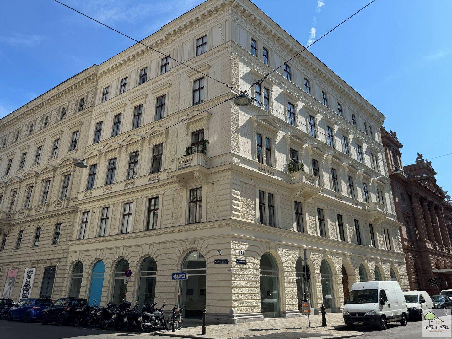 Klassisches Eckgebäude mit historischer Fassade, großen Fenstern und kleinen Balkonen an einer städtischen Straße.