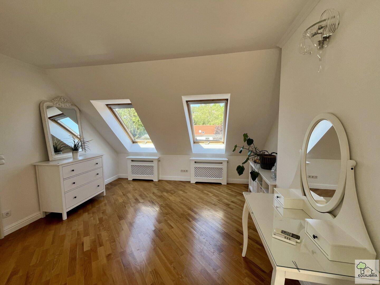 Geräumiger Raum mit Holzfußboden, zwei Dachfenstern und eleganten weißen Möbeln.