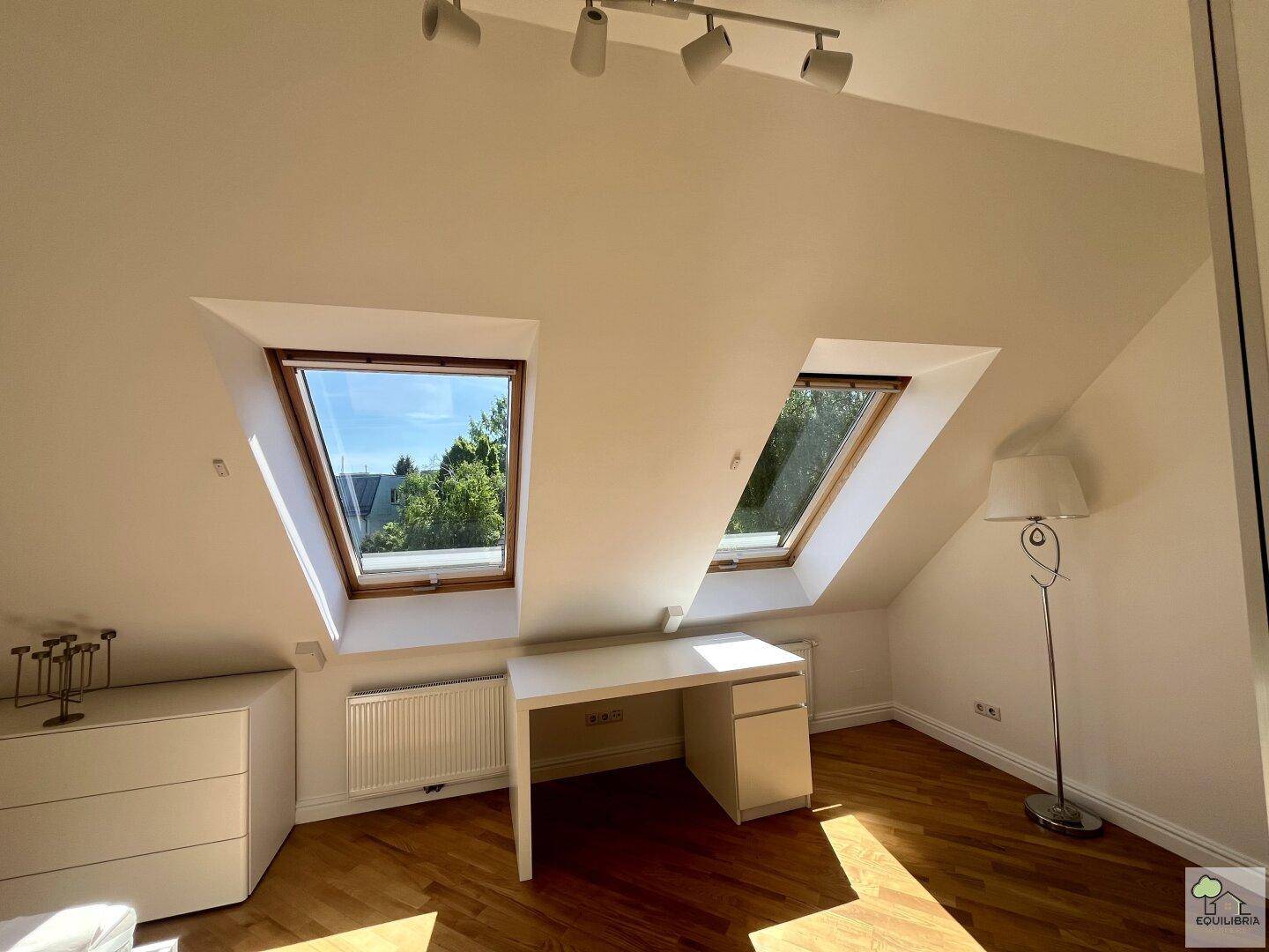 Heller Arbeitsbereich mit zwei Dachfenstern, weißem Schreibtisch und Holzfußboden.