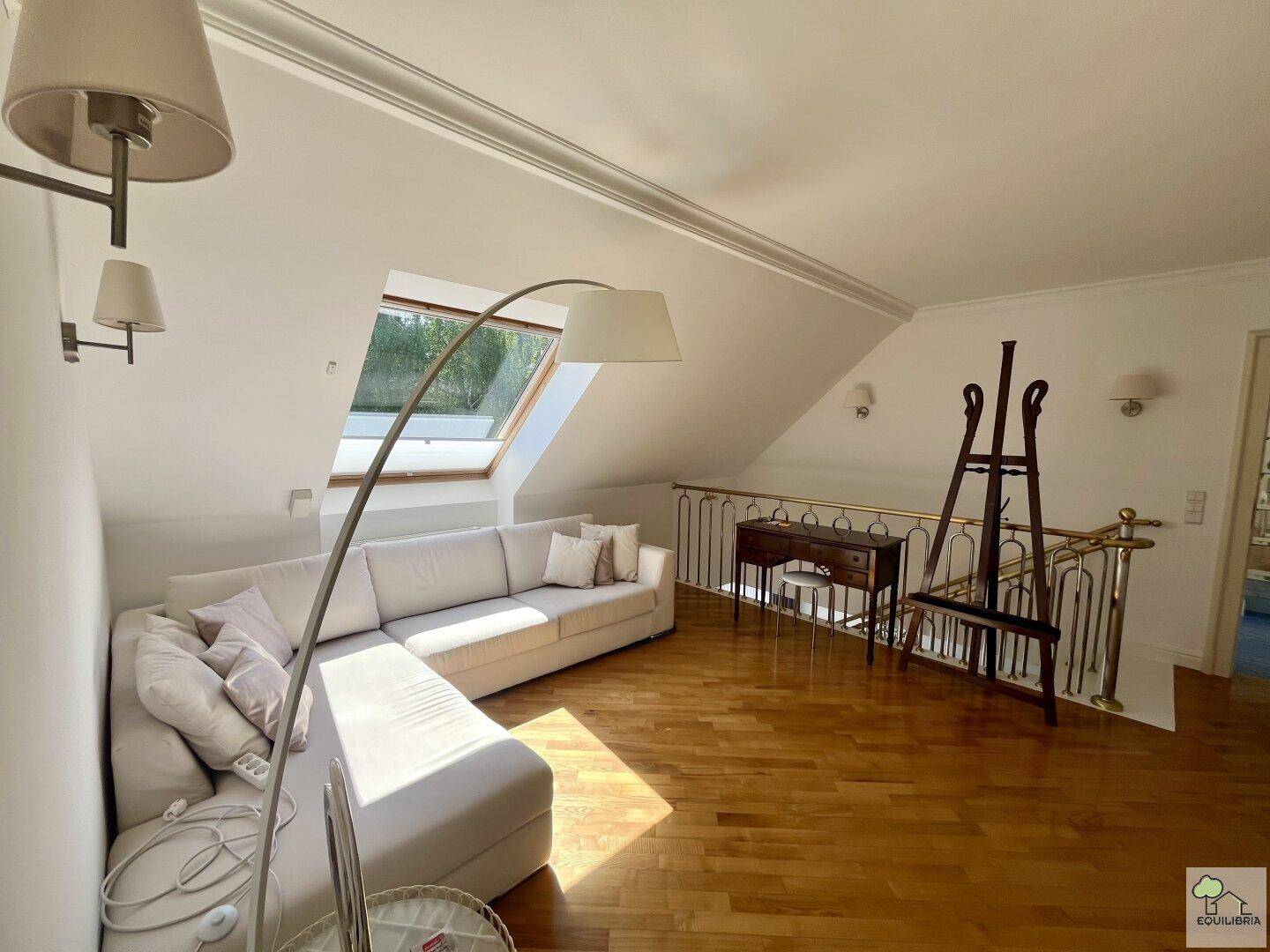 Heller Wohnbereich im Obergeschoss mit bequemer Couch, Dachfenster und Holzfußboden.