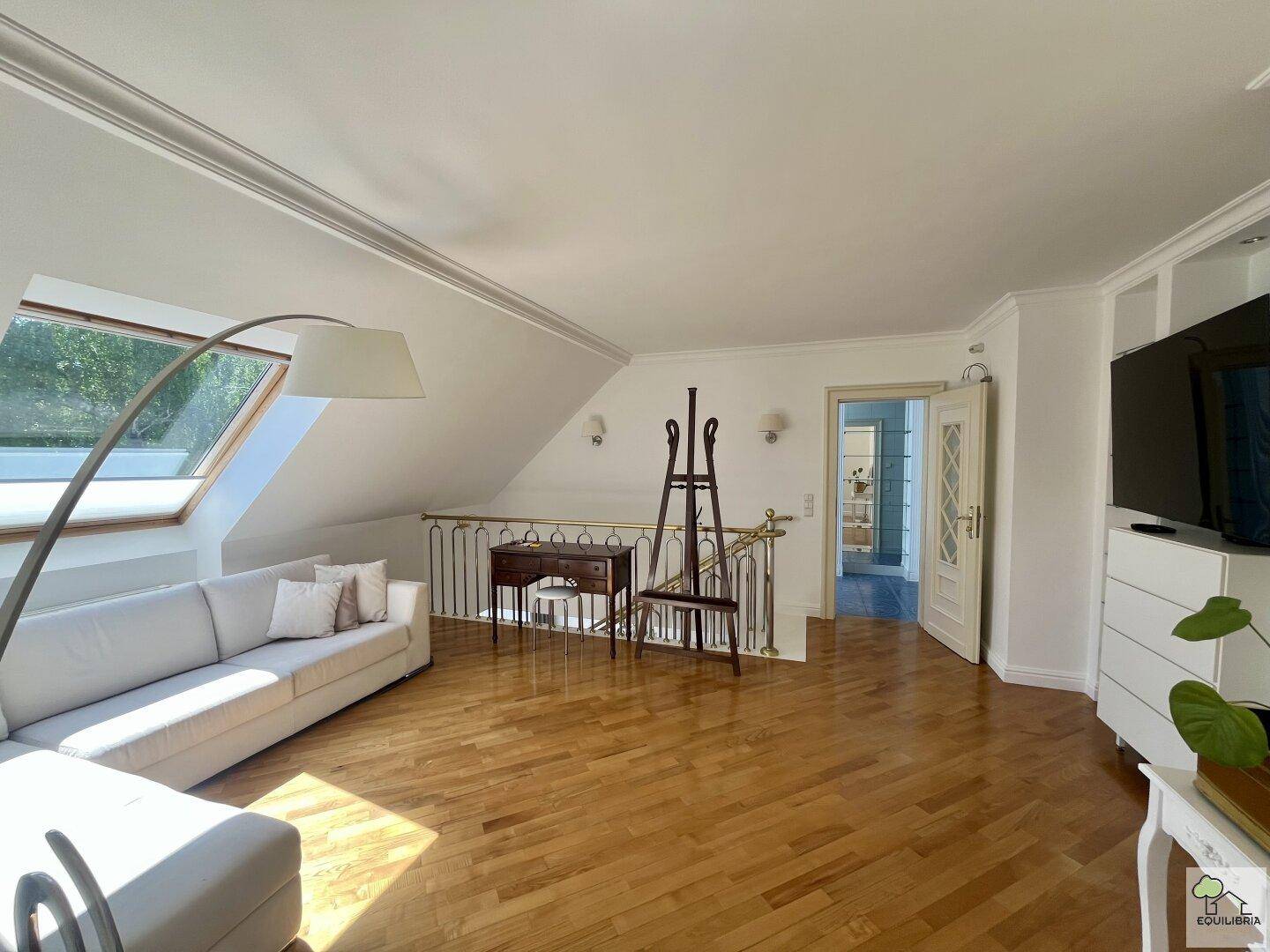 Offener Wohnbereich mit Sofa, Holzfußboden und Dachfenster, das viel Licht spendet.