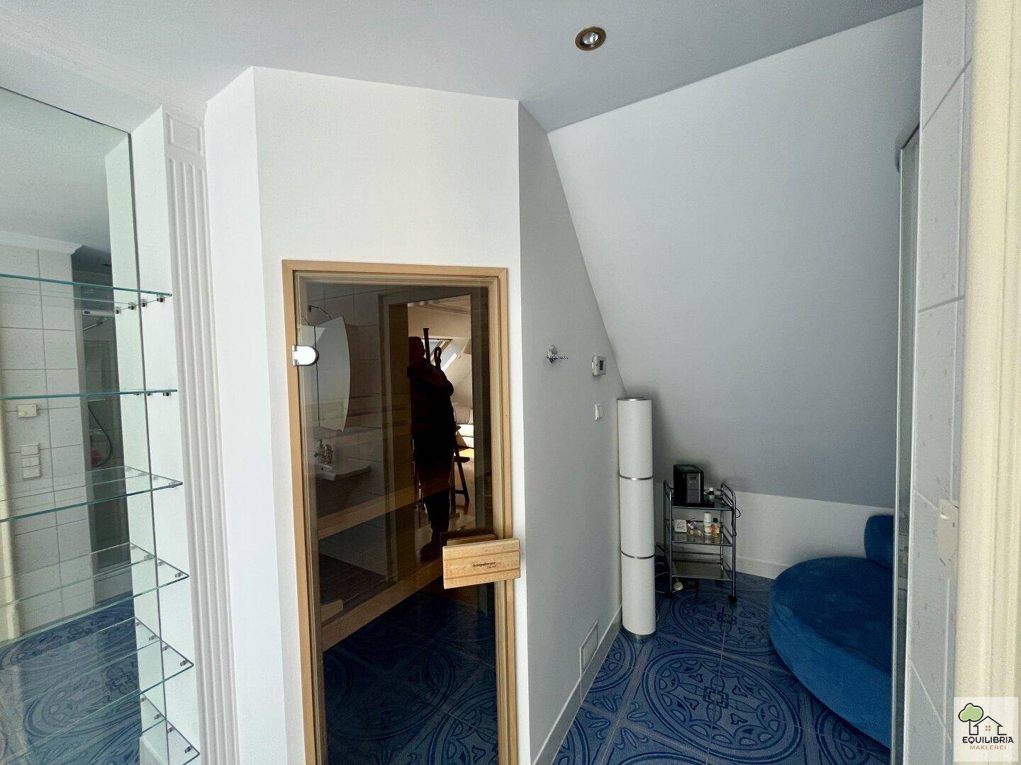 Wellnessbereich mit integrierter Sauna, blauen Fliesen und gemütlicher Sitzecke.