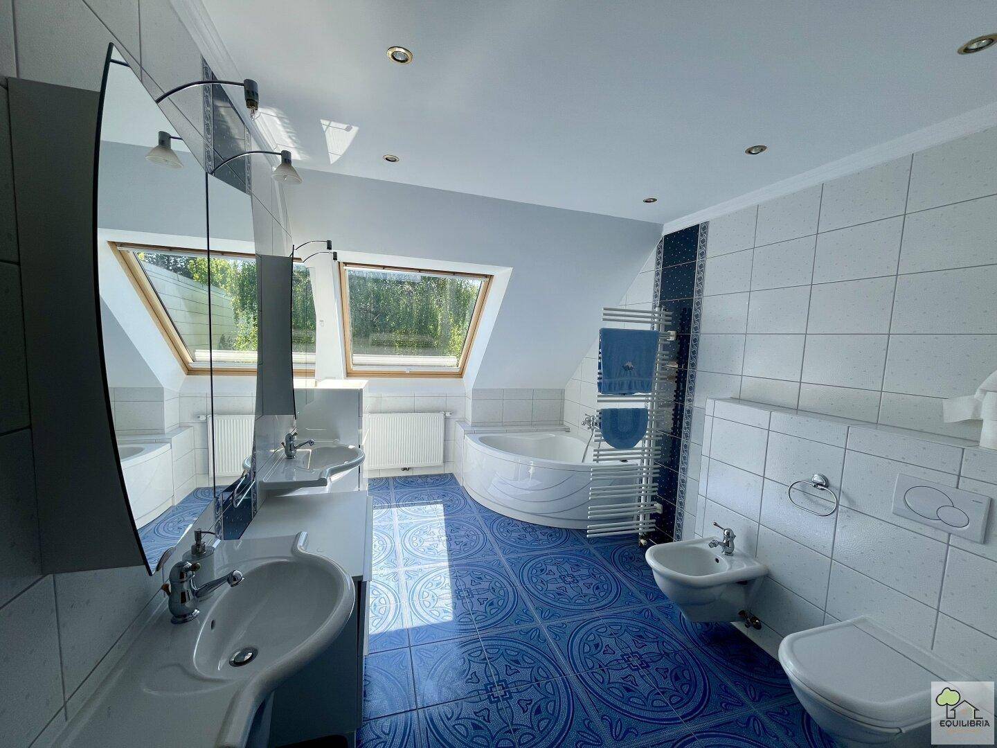 Geräumiges Badezimmer mit blauen Fliesen, Doppelwaschbecken, Eckbadewanne und Dachfenstern.