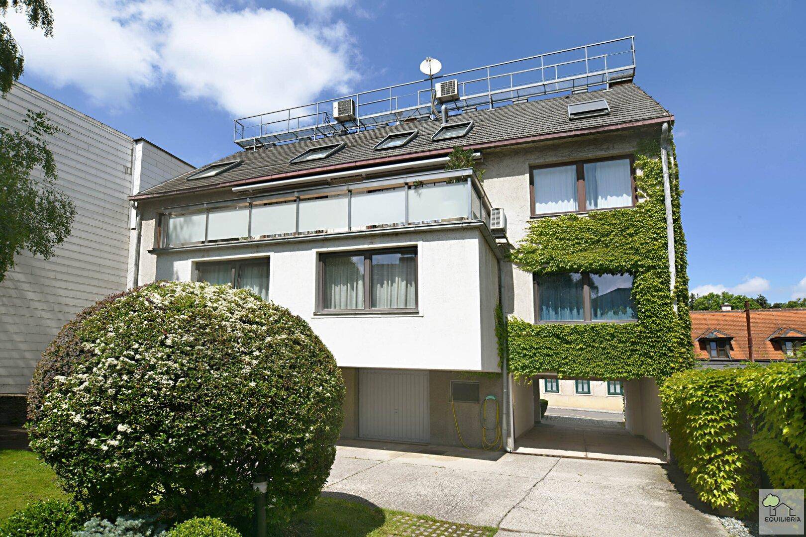 Mehrstöckiges Gebäude mit begrüntem Gartenbereich, Balkon und einer Dachterrasse.