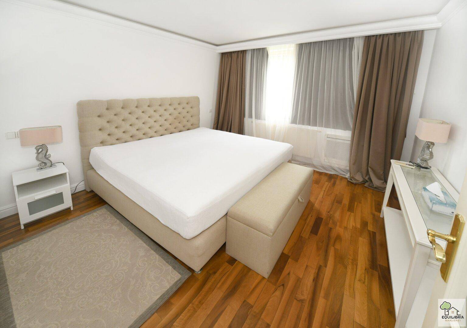 Gemütliches Schlafzimmer mit Parkettboden, einem großen Bett und hellen Vorhängen am Fenster.