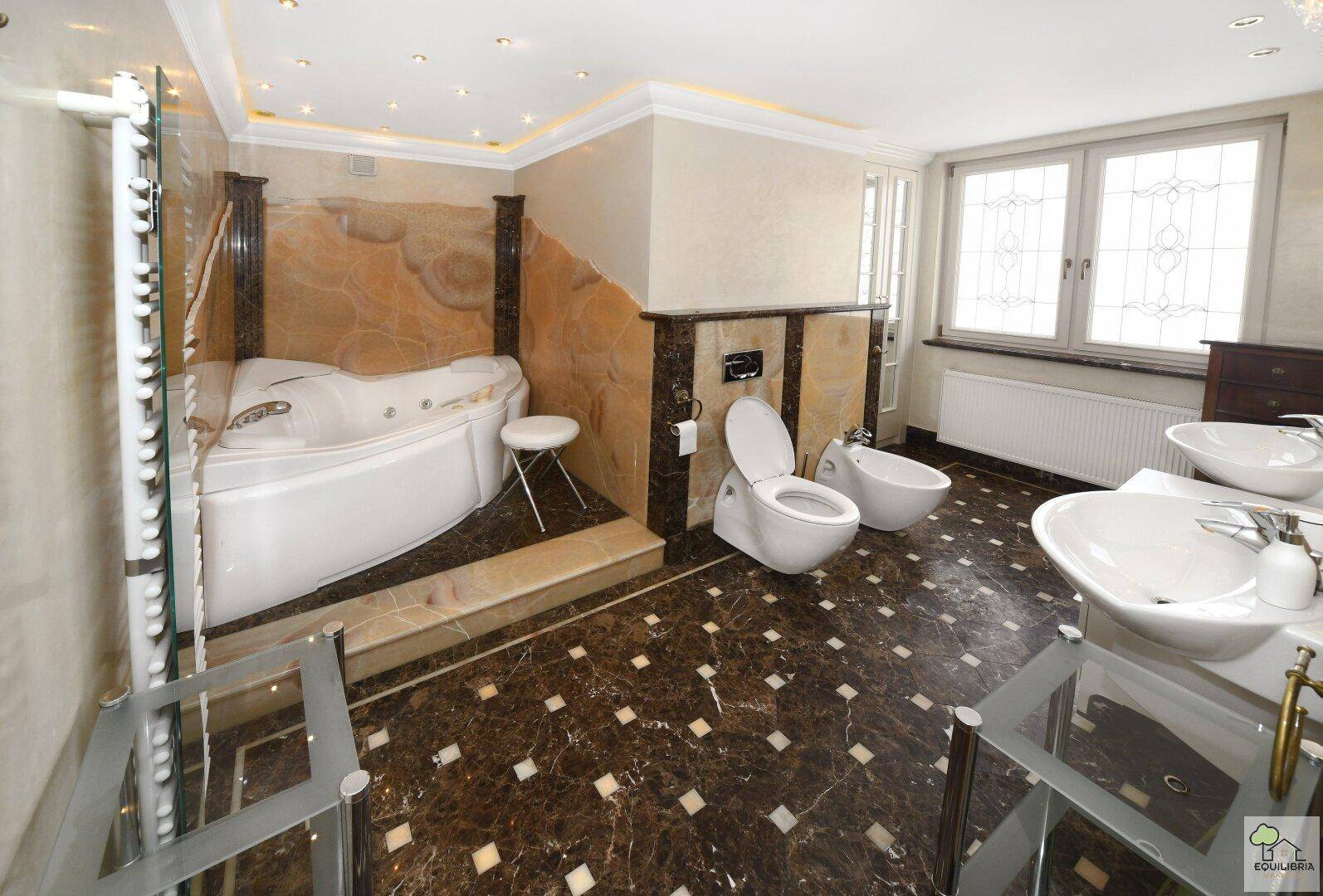 Luxuriöses Badezimmer mit Whirlpool, dunklem Marmorboden und doppelten Waschbecken.