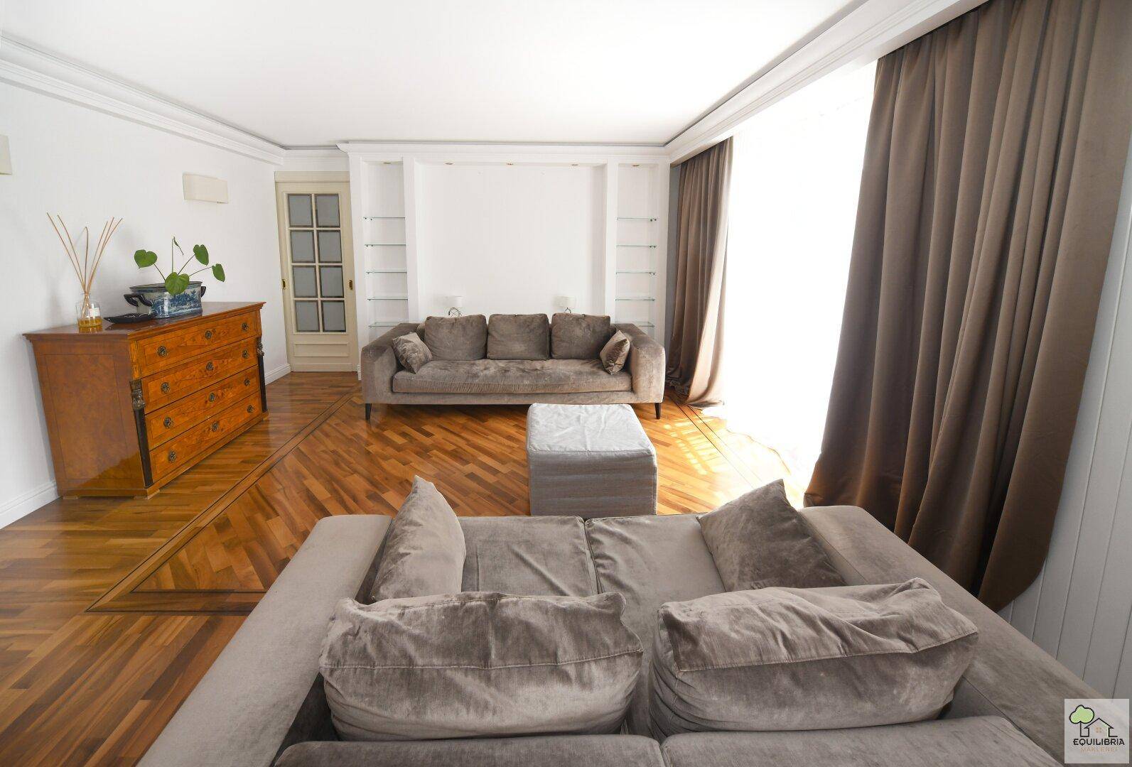 Geräumiges Wohnzimmer mit Parkettboden, bequemen Sofas und großen Fenstern mit viel Tageslicht.