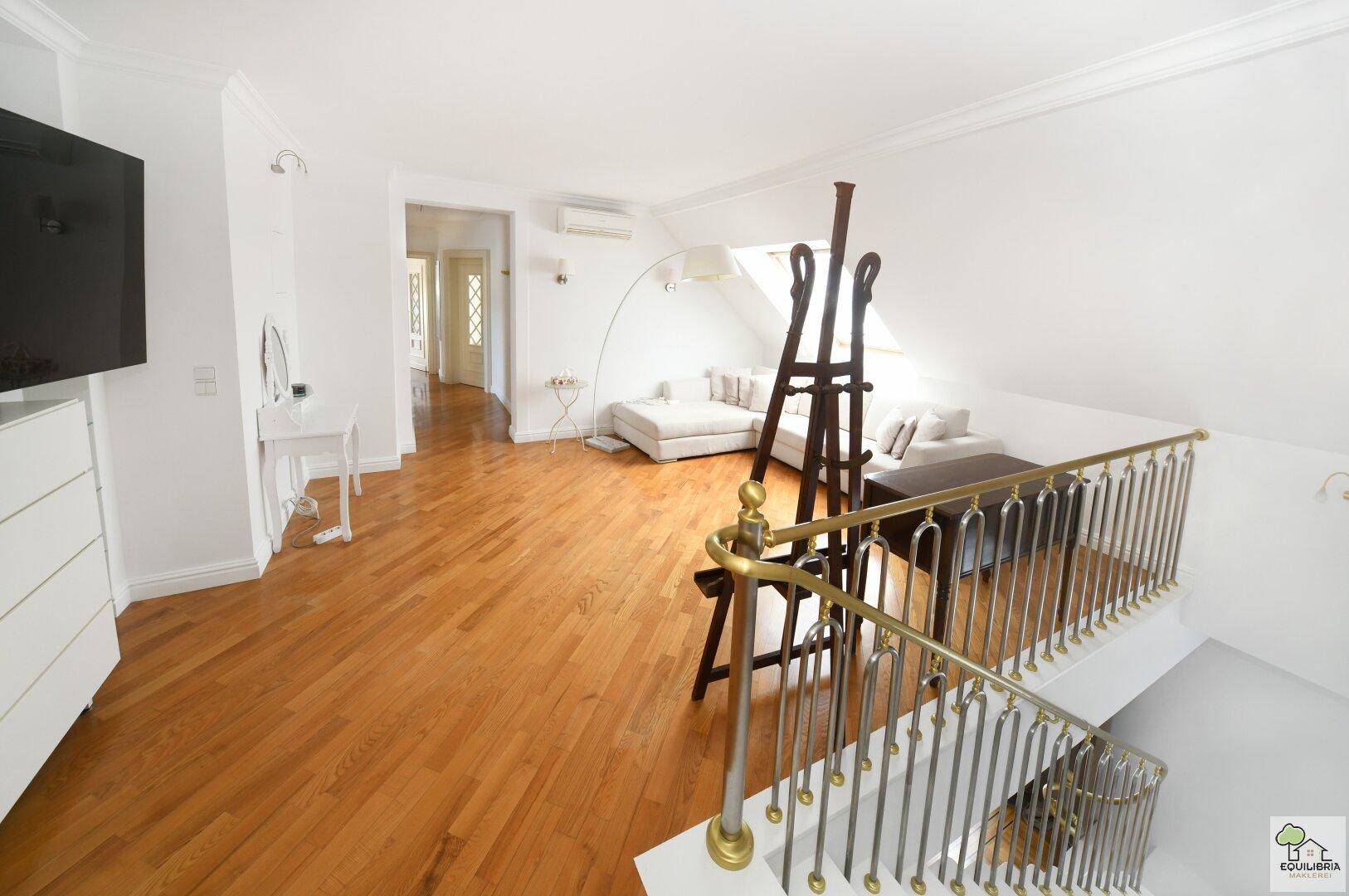 Offener Wohnbereich im Dachgeschoss mit Holzboden, eleganter Treppe und viel Tageslicht.