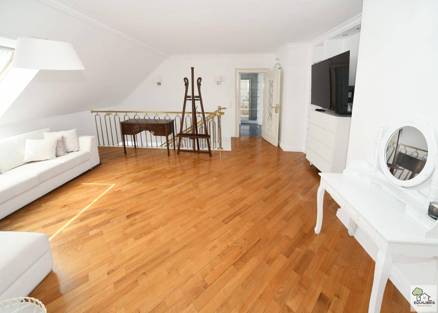 Geräumiger Wohnbereich im Dachgeschoss mit Holzboden, weißem Sofa und Schminktisch.