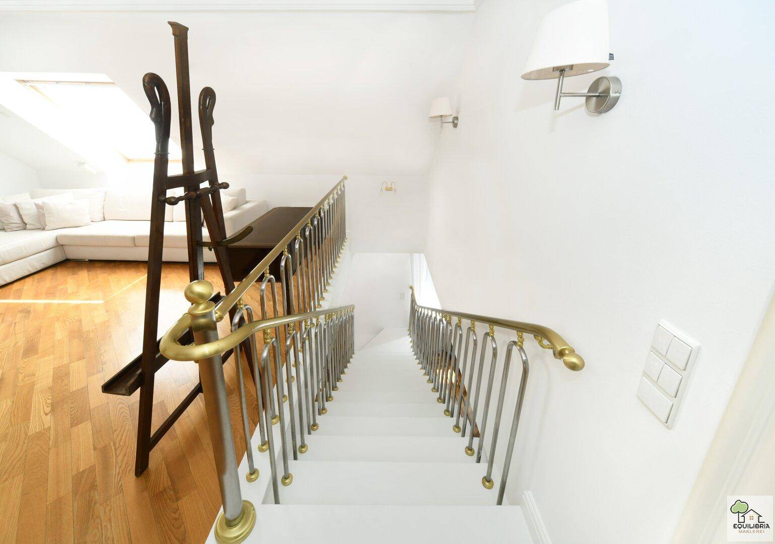 Elegante Treppe mit goldenem Handlauf, die in den oberen Wohnbereich führt.