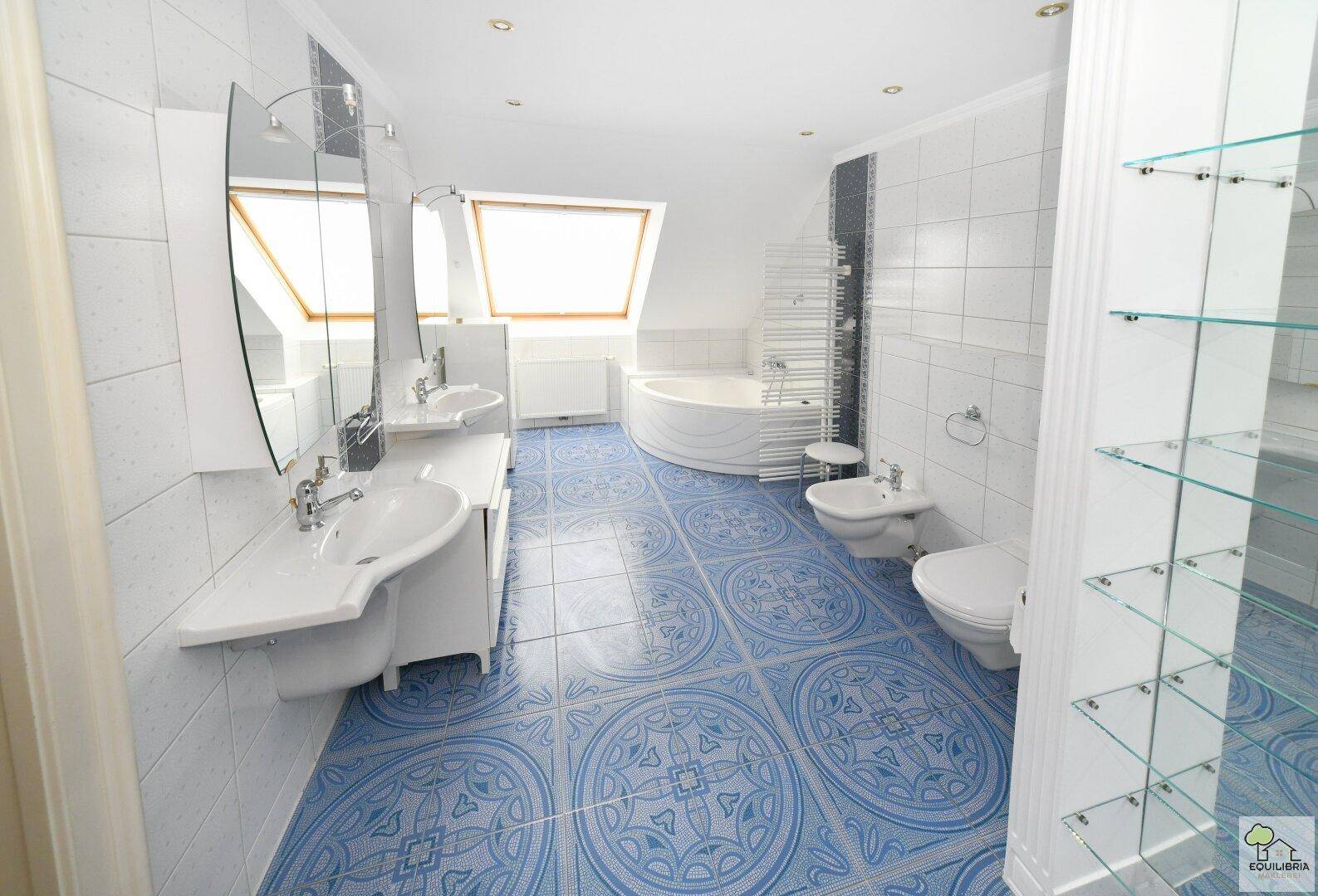Modernes Badezimmer im Dachgeschoss mit blauen Fliesen, Badewanne und Doppelwaschbecken.