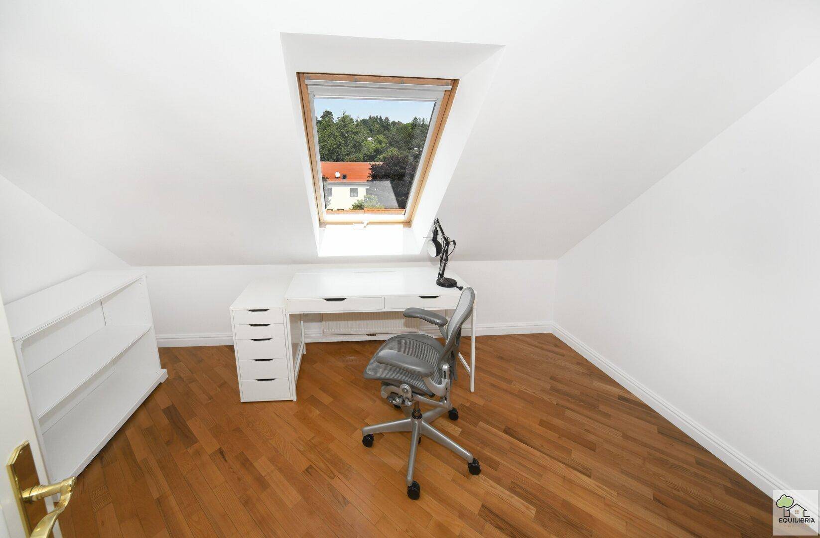 Helles Büro im Dachgeschoss mit Holzboden, Schreibtisch und Dachfenster.