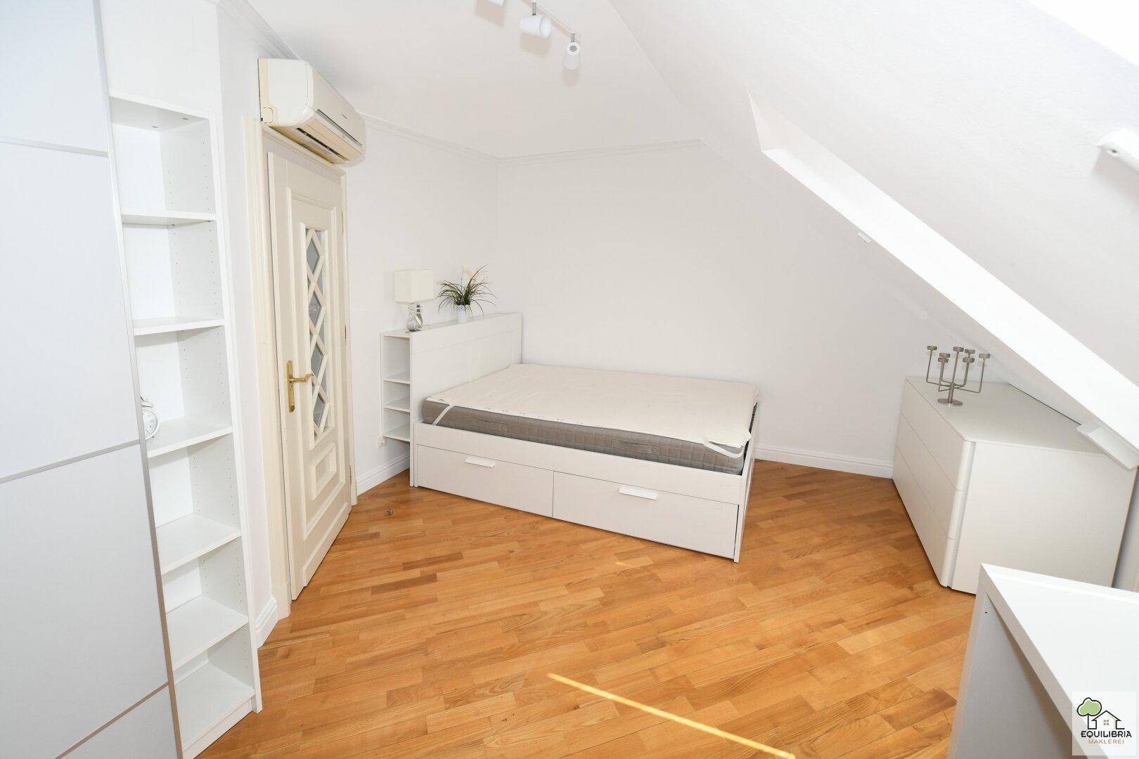 Helles Schlafzimmer im Dachgeschoss mit Holzboden, Klimaanlage und weißem Kleiderschrank.
