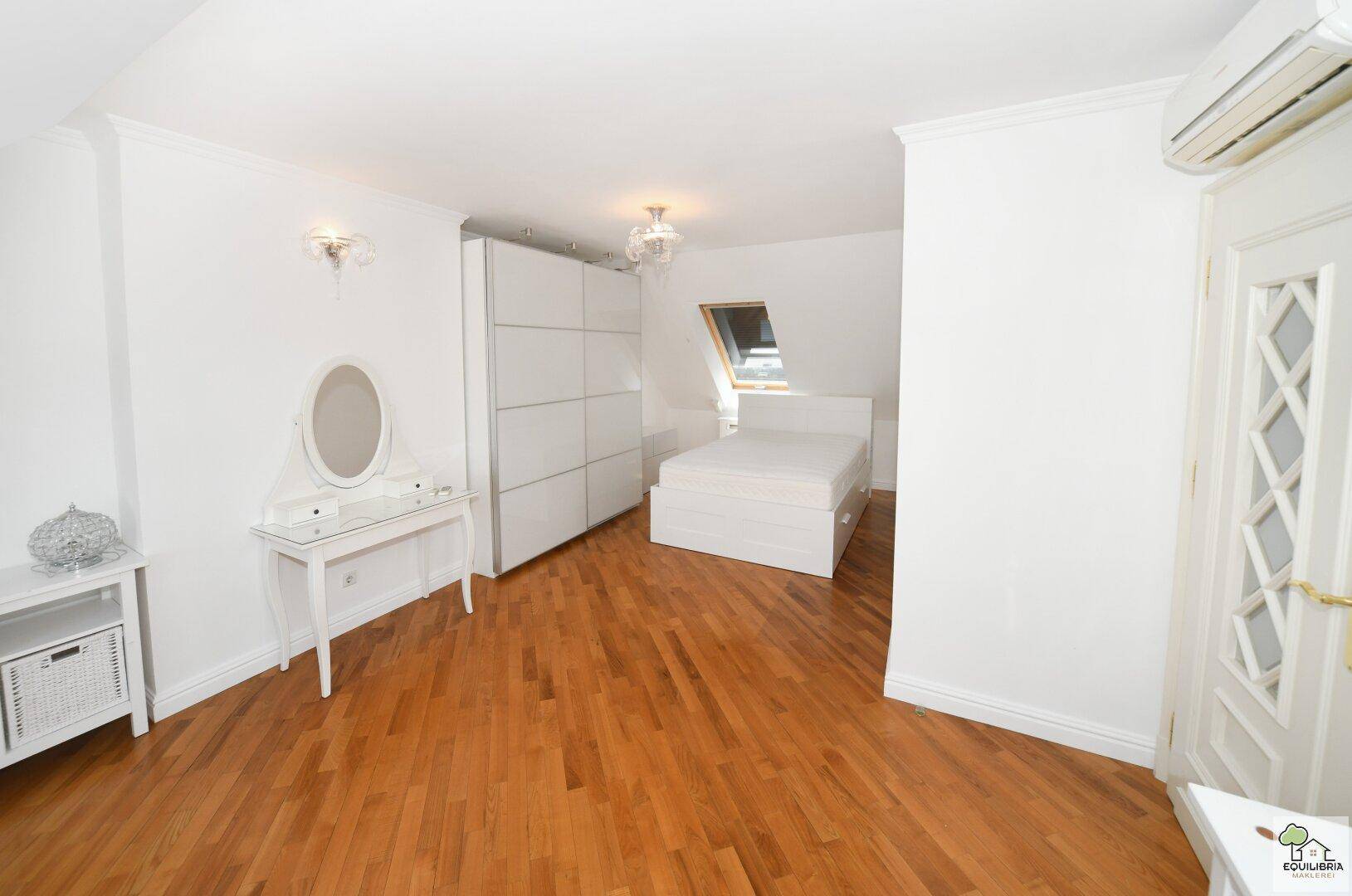 Geräumiges Schlafzimmer im Dachgeschoss mit Holzboden, weißem Mobiliar und großem Kleiderschrank.