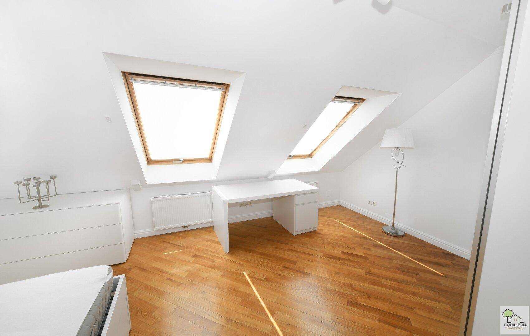 Lichtdurchflutetes Dachzimmer mit zwei Dachfenstern, Holzboden und einem modernen Schreibtisch.