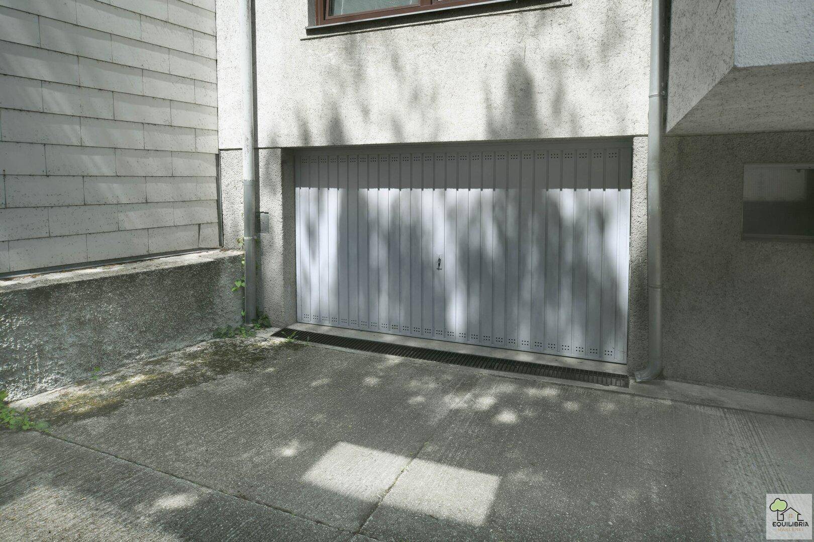 Außenansicht der Garage mit Zufahrt und modernem Garagentor in hellem Grau.
