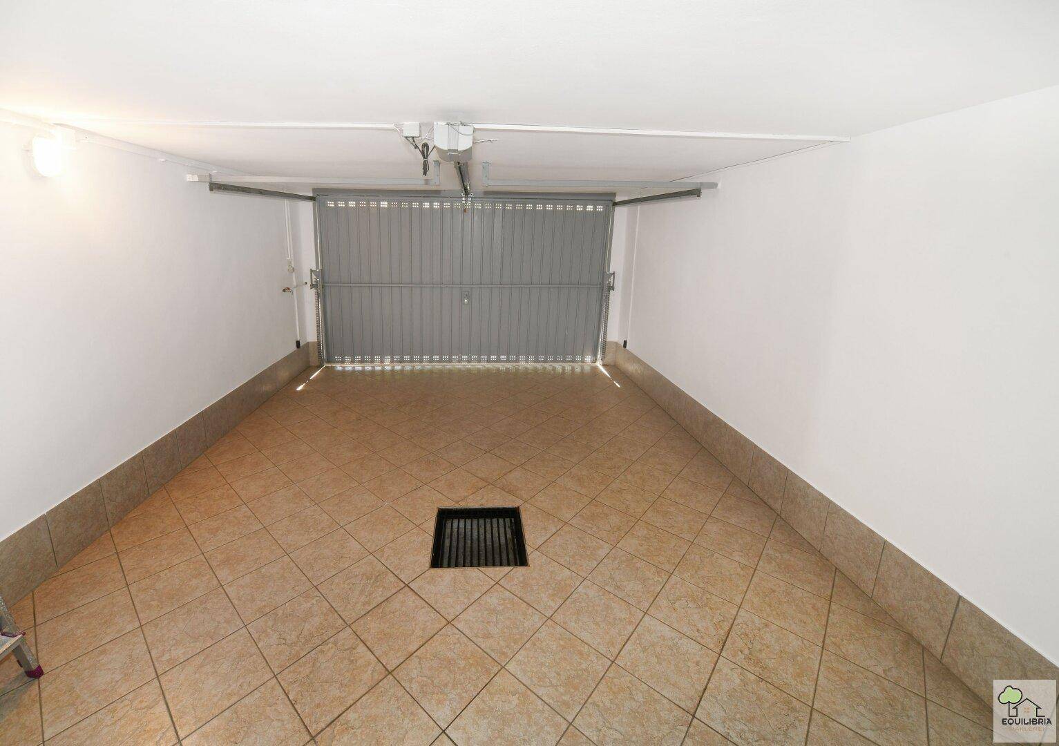 Geräumige Garage mit Fliesenboden und automatischem Garagentor für ein Fahrzeug.